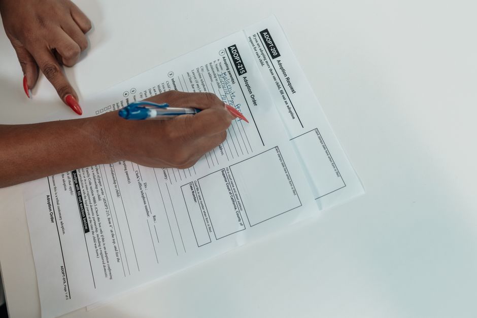 Close-up of a hand filling out an adoption request form with a pen.